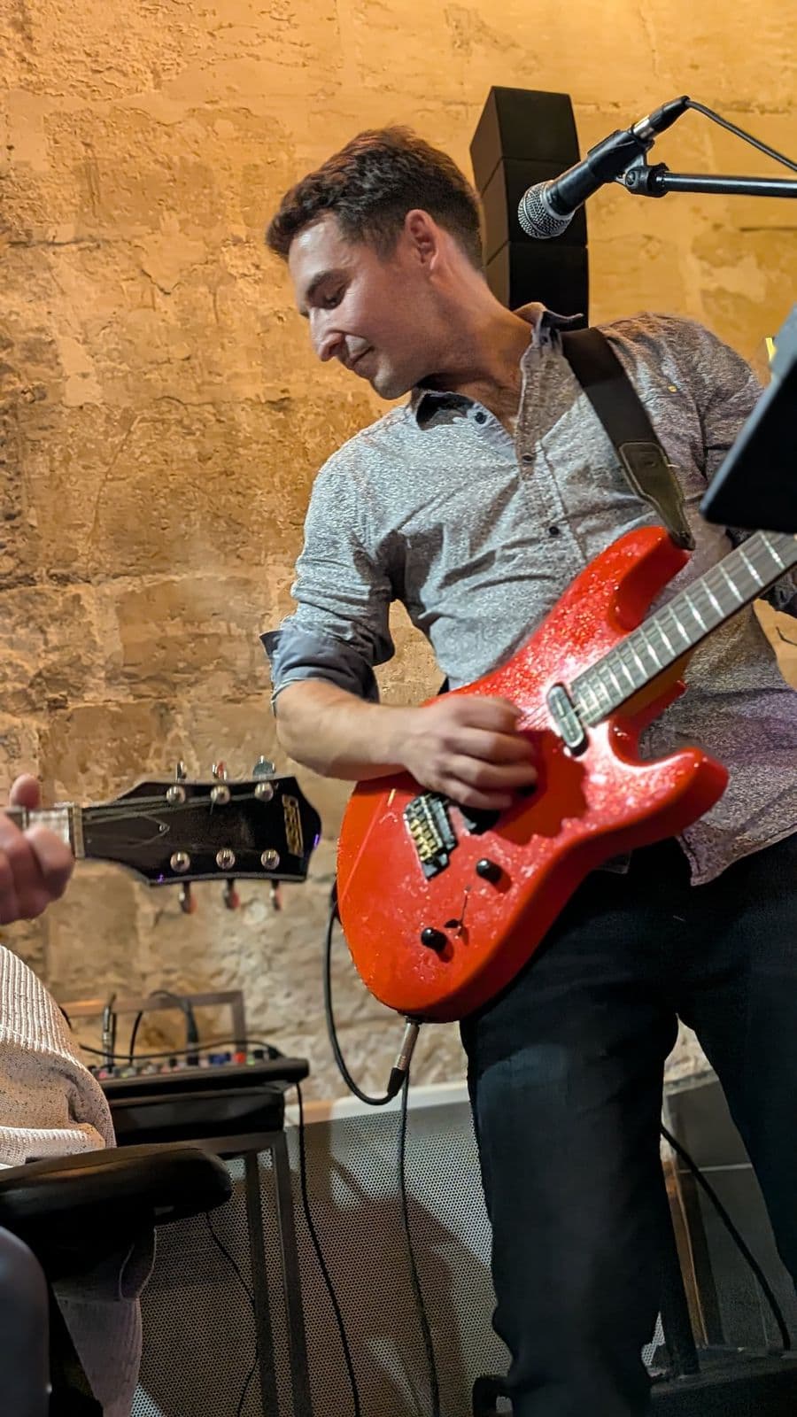 Guitariste à la guitare rouge pendant un concert, mur de pierre éclairé