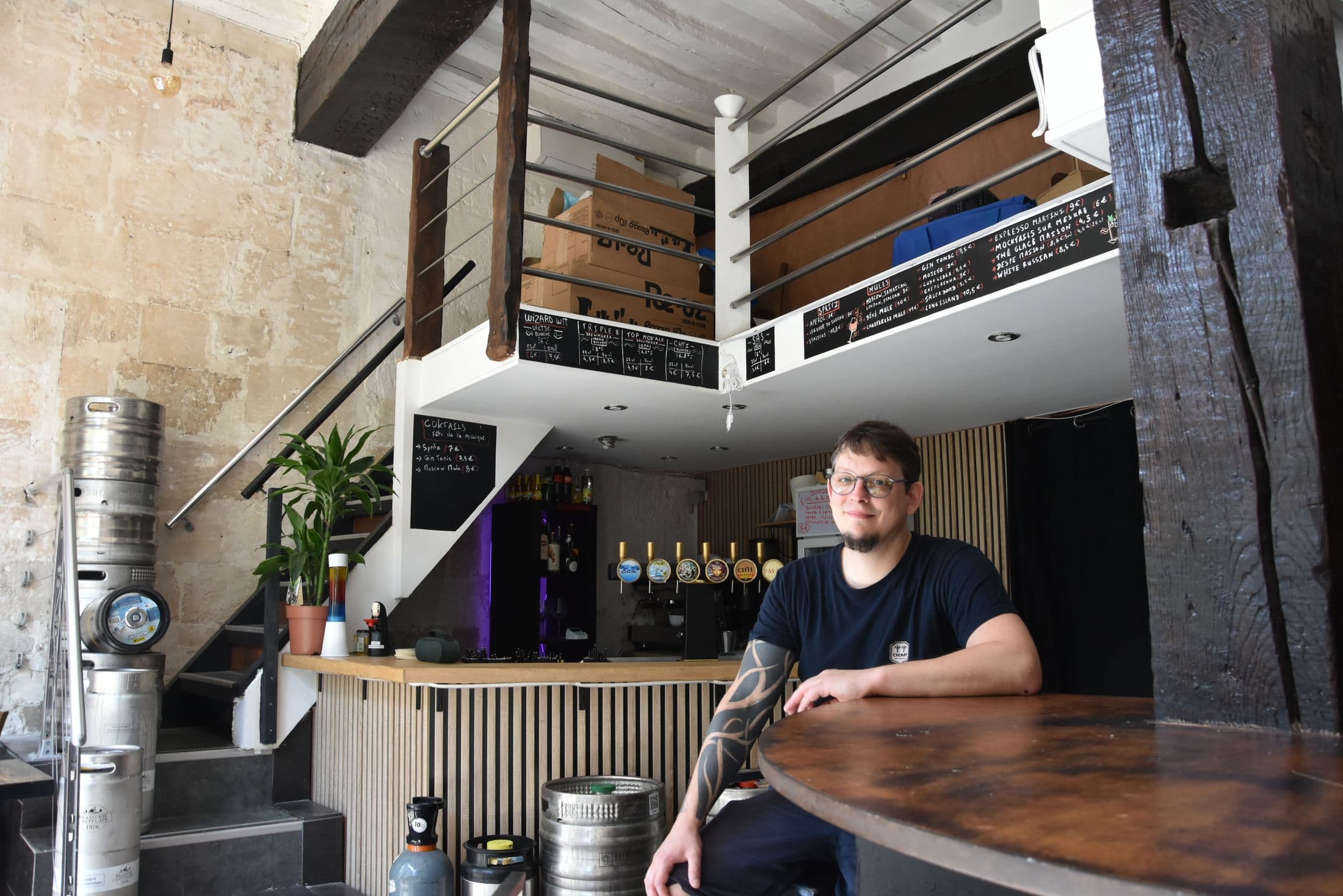 La salle du Bec : murs en pierre, escalier vers la mezzanine, fûts et comptoir aux cinq tireuses