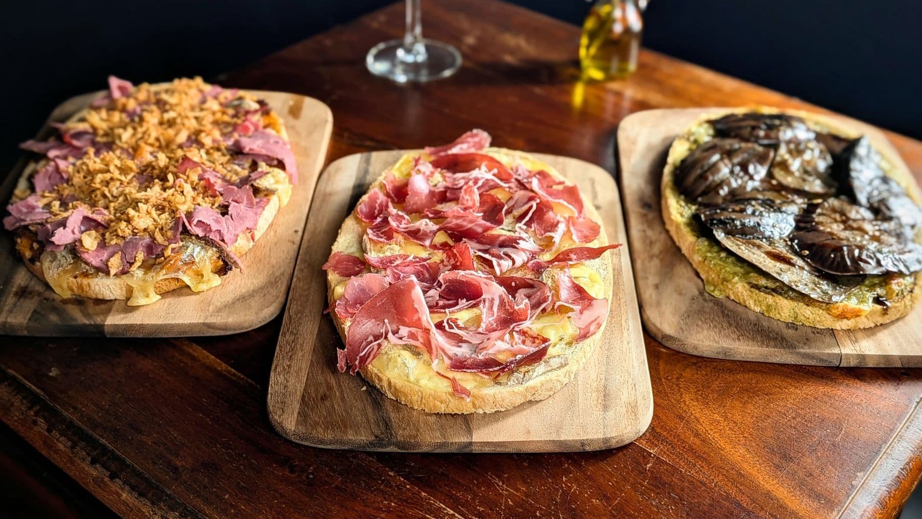 Trois tartines gratinées sur planches de bois : aubergine, jambon cru, pastrami